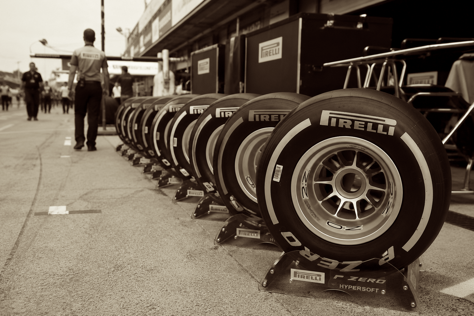 Fila de neumáticos Pirelli alineados sobre sus soportes en el pit lane de un Gran Premio, con un operario caminando al fondo